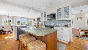 A modern kitchen with a central island, white cabinetry, and a microwave. - Coastal Farmhouse Retreat in Little Compton, RI – Your Perfect Seaside Getaway (Little Compton)