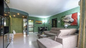 A spacious living room with a beige sofa set, a dining area, and a kitchen visible through an open doorway. - Green house (Monopoli)