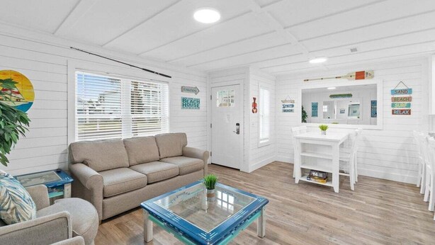 Un salón amplio con un sofá color beige, una mesa de centro de vidrio y una zona de comedor blanca.