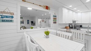 Una cocina moderna con armarios blancos, un espejo grande y un comedor con mesa y sillas blancas.