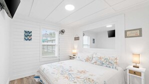 Un dormitorio con cama, dos mesitas de noche, televisor y ventana con persianas.