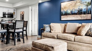 A modern living room with a beige sofa, a patterned rug, and a dining area with a table and chairs. - Roark Downtown Branson, Pools, Playground! (Branson)