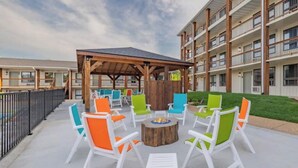 An outdoor patio with white and colorful chairs, a wooden table, and a fire pit. - Roark Downtown Branson, Pools, Playground! (Branson)