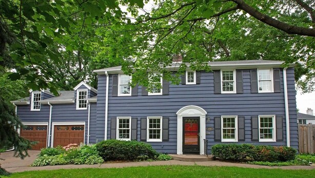 Una casa de dos pisos con fachada azul oscuro, detalles blancos y puerta roja.