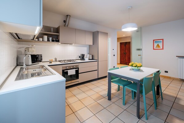 A modern kitchen with white cabinets, a gas stove, and a sink. There is a dining table with chairs and a vase of flowers.