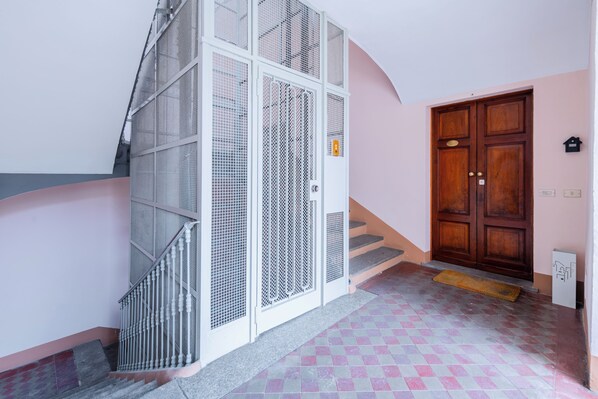 Una escalera con barandilla de metal, una puerta de madera y piso de baldosas.