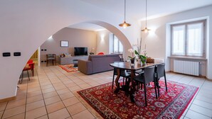 Ein modernes Wohnzimmer mit Fernseher, einer Couch, einem Esstisch und Stühlen, angrenzend an eine Küche.