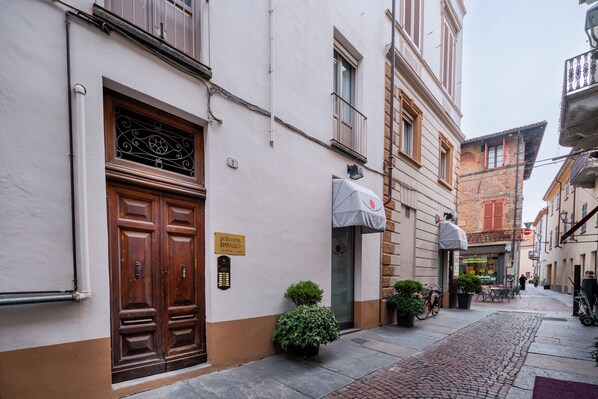 A narrow street with a building featuring a double wooden door, a small potted plant, and a sign indicating a restaurant.