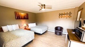 A hotel room with two beds, a ceiling fan, a wooden floor, a small trash bin, and a microwave on a wooden counter.