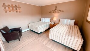Ein Hotelzimmer mit zwei Betten, einem Sessel, einem Nachttisch mit Lampe und einer Wanddekoration.