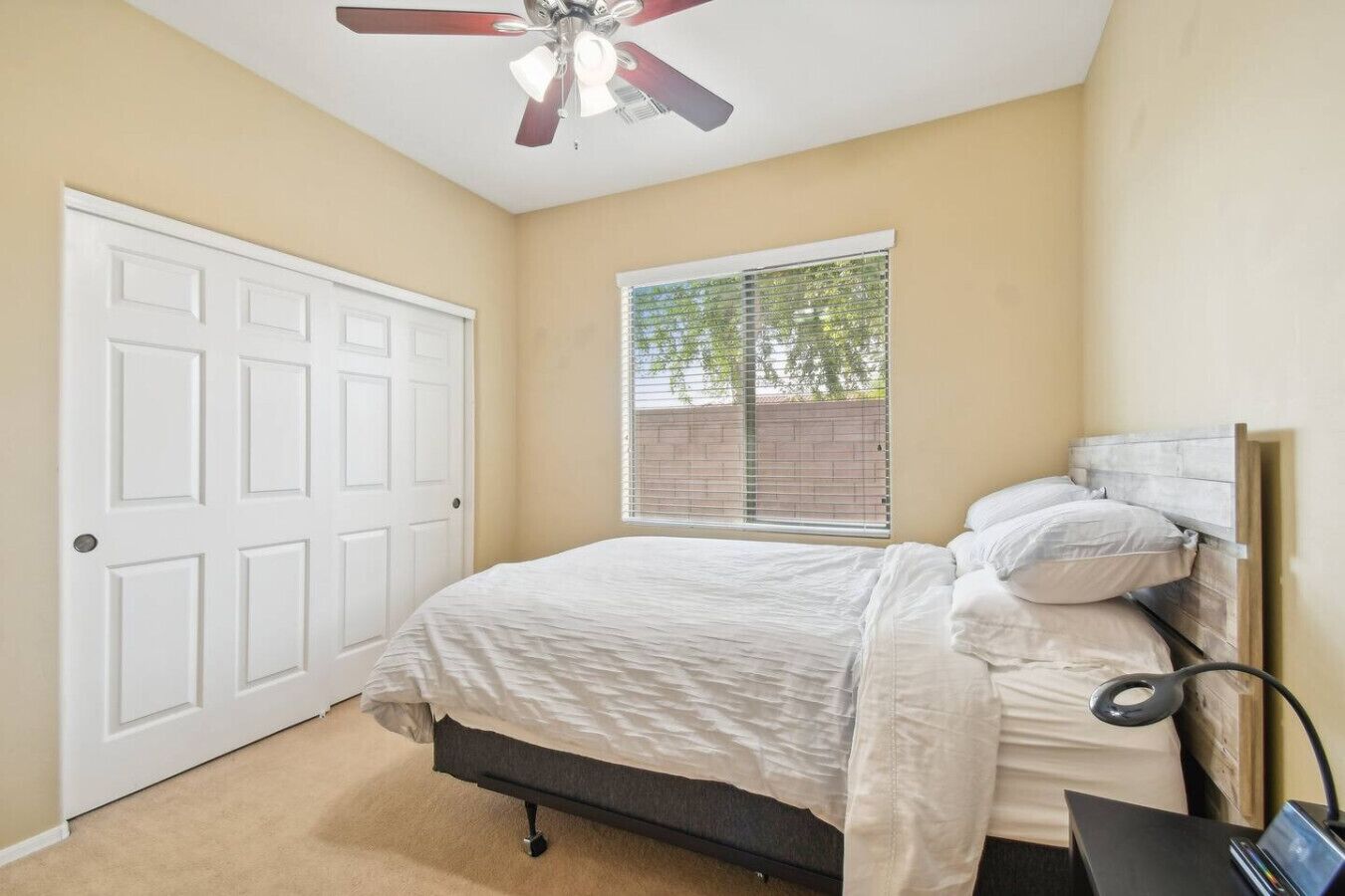 A bedroom with a bed, a ceiling fan, a window with blinds, and a door.
