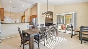 A modern kitchen with a dining area, featuring a large wooden table and chairs, a built-in oven, and a hanging light fixture.