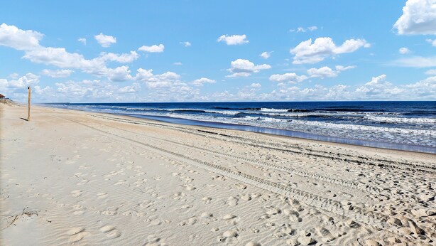 Une plage de sable où l’on peut voir des empreintes de pas qui mènent à l’océan.