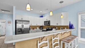 Une cuisine moderne avec des meubles blancs, des appareils en acier inoxydable, un îlot central doté de tabourets et un éclairage suspendu.