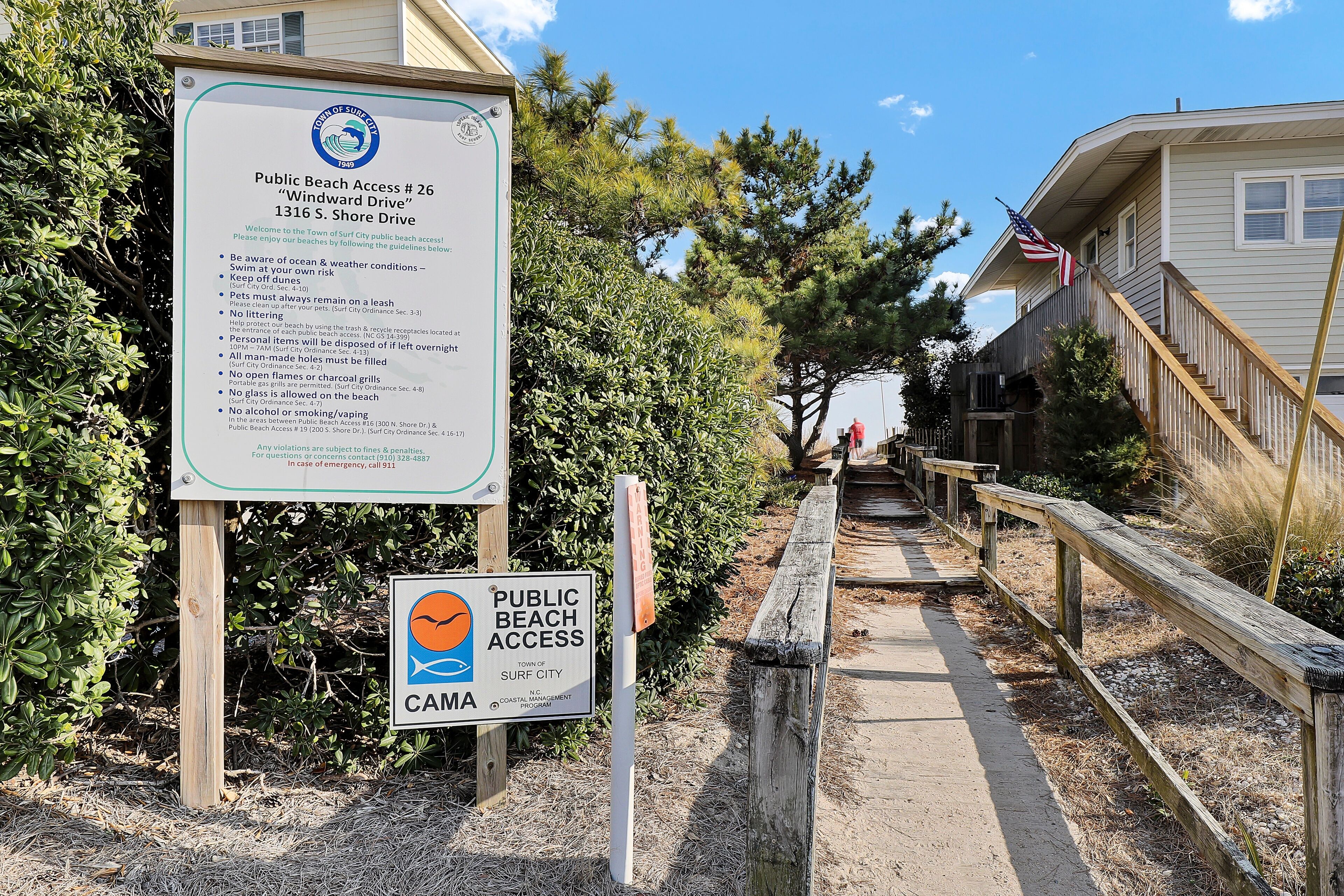 A beach access sign with guidelines and a wooden walkway leading to a beach area.