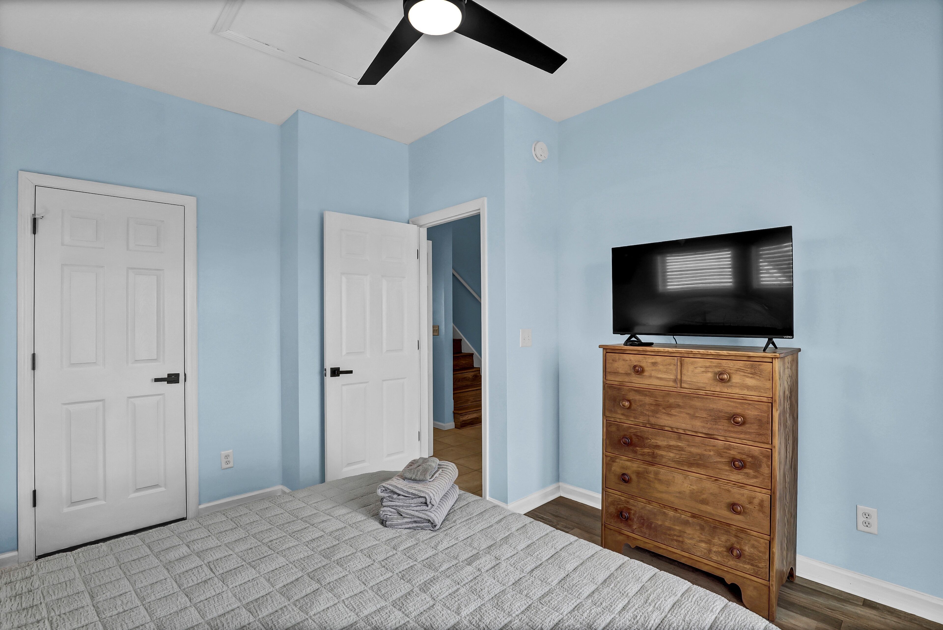 A bedroom with a bed, a dresser, a television, and a ceiling fan.