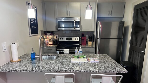 A kitchen with granite countertops, stainless steel appliances, and white bar stools. - King Suite | 1mi to The Battery + Mins to Midtown! (Atlanta)
