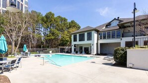 A swimming pool with lounge chairs, a covered seating area, and a building with large windows and a balcony. - King Suite | 1mi to The Battery + Mins to Midtown! (Atlanta)