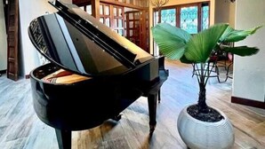 Un piano à queue se trouve dans une pièce spacieuse et bien éclairée, dotée d’une grande fenêtre et d’une plante en pot.