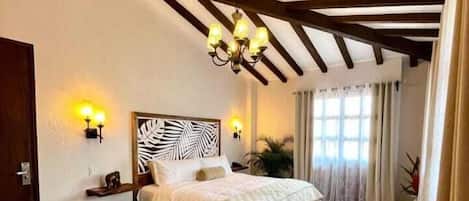 A bedroom with a wooden floor, a bed with a white headboard, two wall-mounted lamps, and a chandelier.