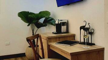 Un escritorio de madera con una silla, una planta en maceta, una copa de vino y un televisor fijado en la pared.