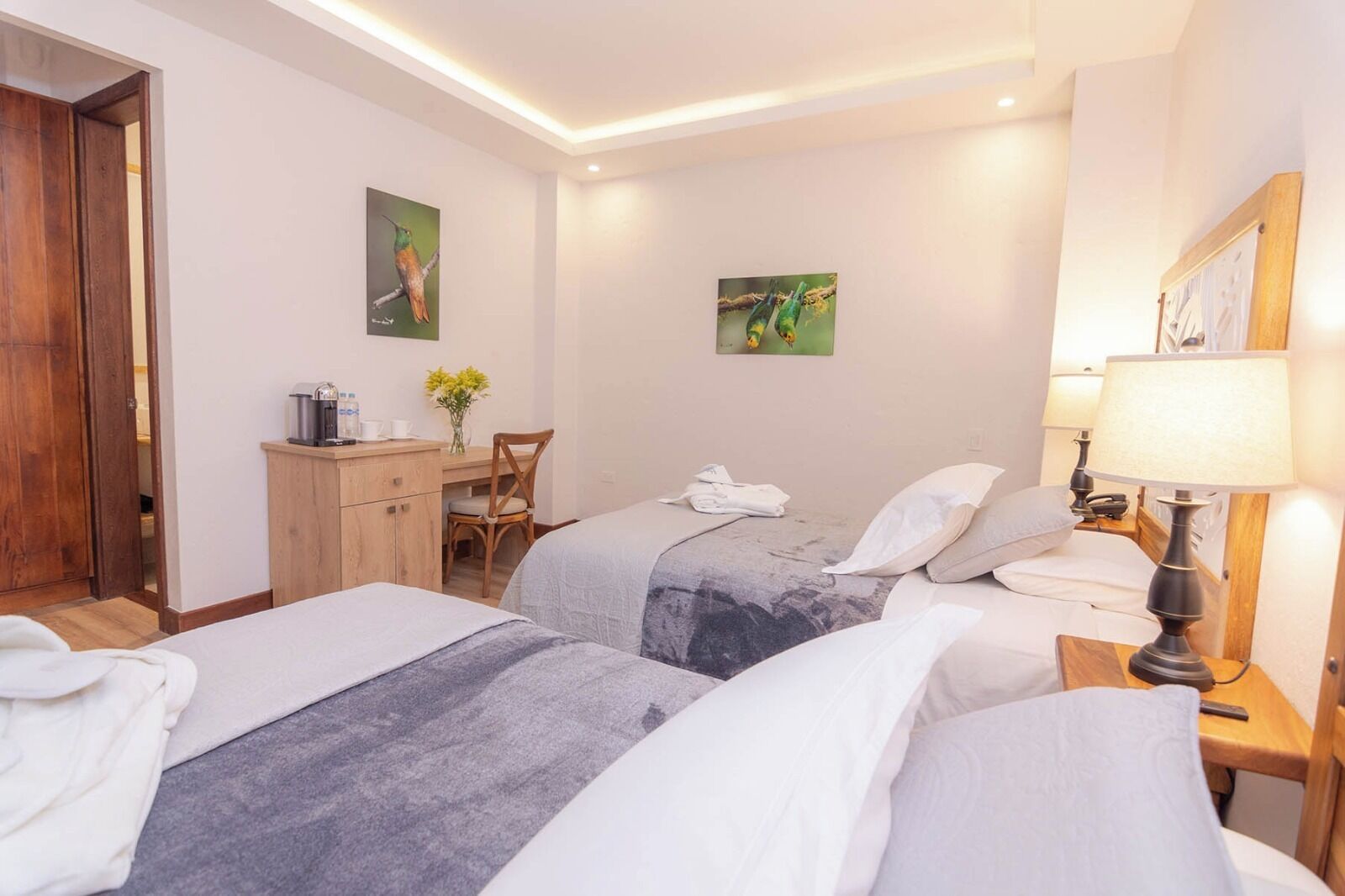 A hotel room with two beds, a desk, a chair, a lamp, and artwork on the walls.