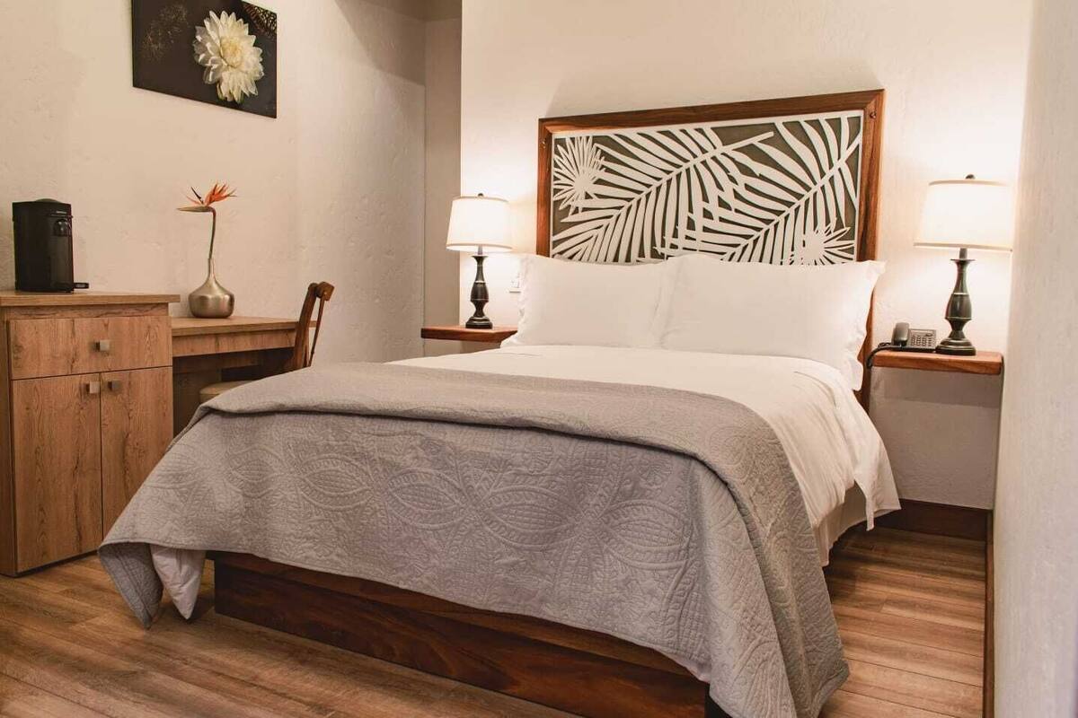 A neatly arranged bedroom with a bed, bedside tables, a nightstand, a wooden dresser, and a wall-mounted artwork.