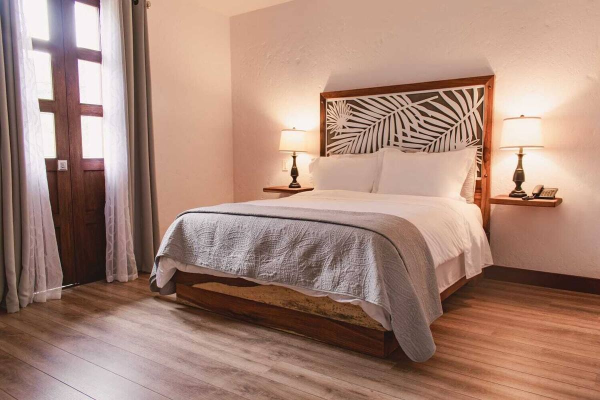 A neatly made bed with a patterned bedspread, two bedside lamps, and a decorative wall panel.
