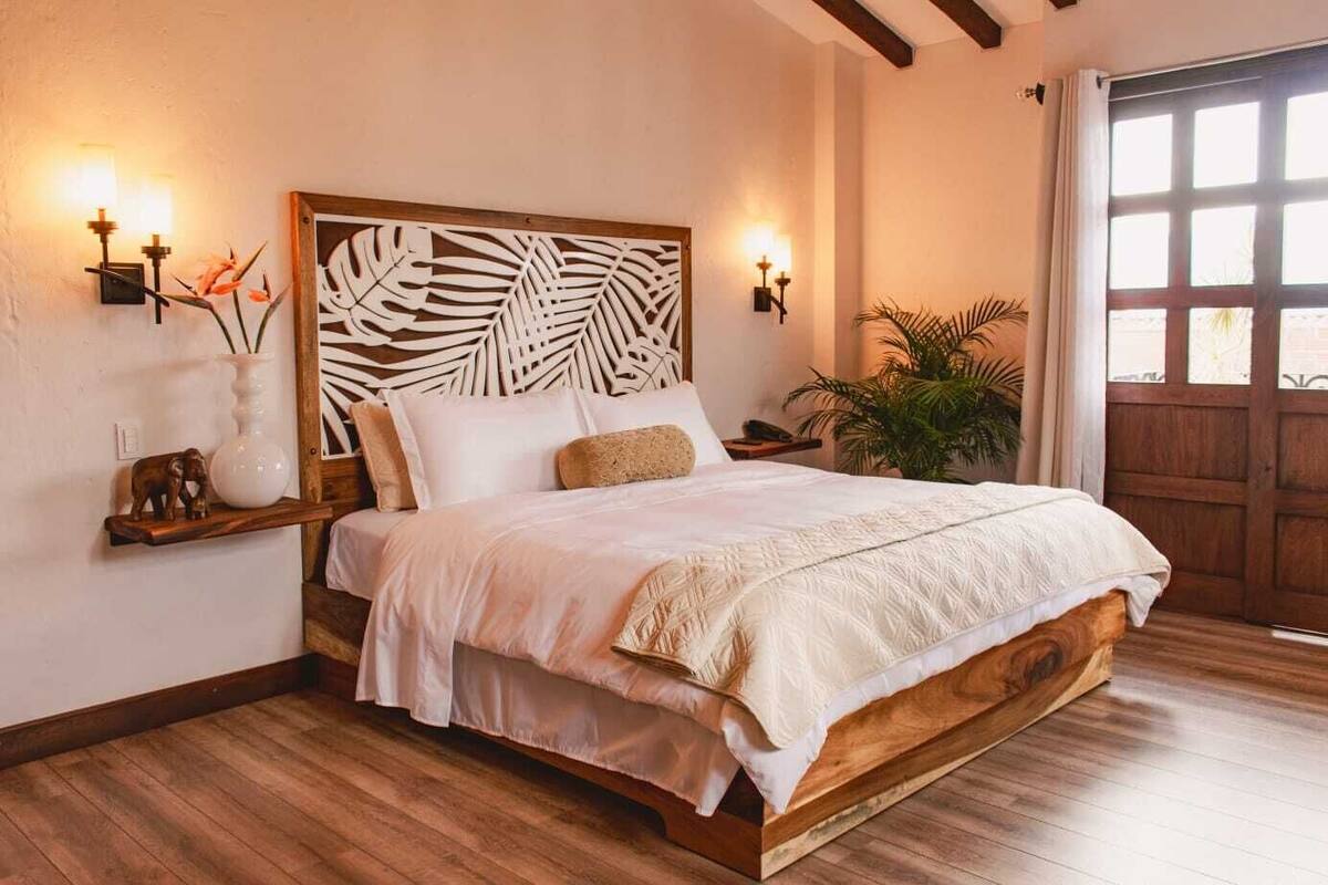 A bedroom with a wooden bed frame, a leaf-patterned headboard, and bedside lamps.