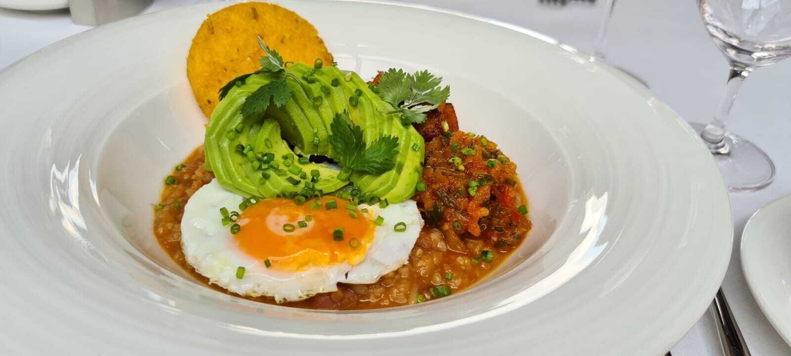 A plate of food with an egg, avocado, and a side dish, served on a white plate.