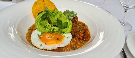 Un plato de comida con un huevo, aguacate y un acompañamiento, servido sobre un plato blanco.