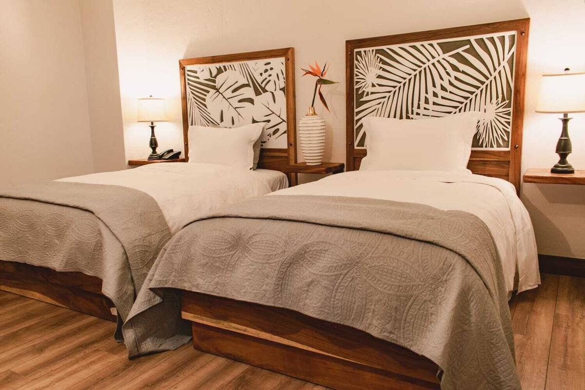 A hotel room with two beds, wooden headboards, and a nightstand with a lamp.