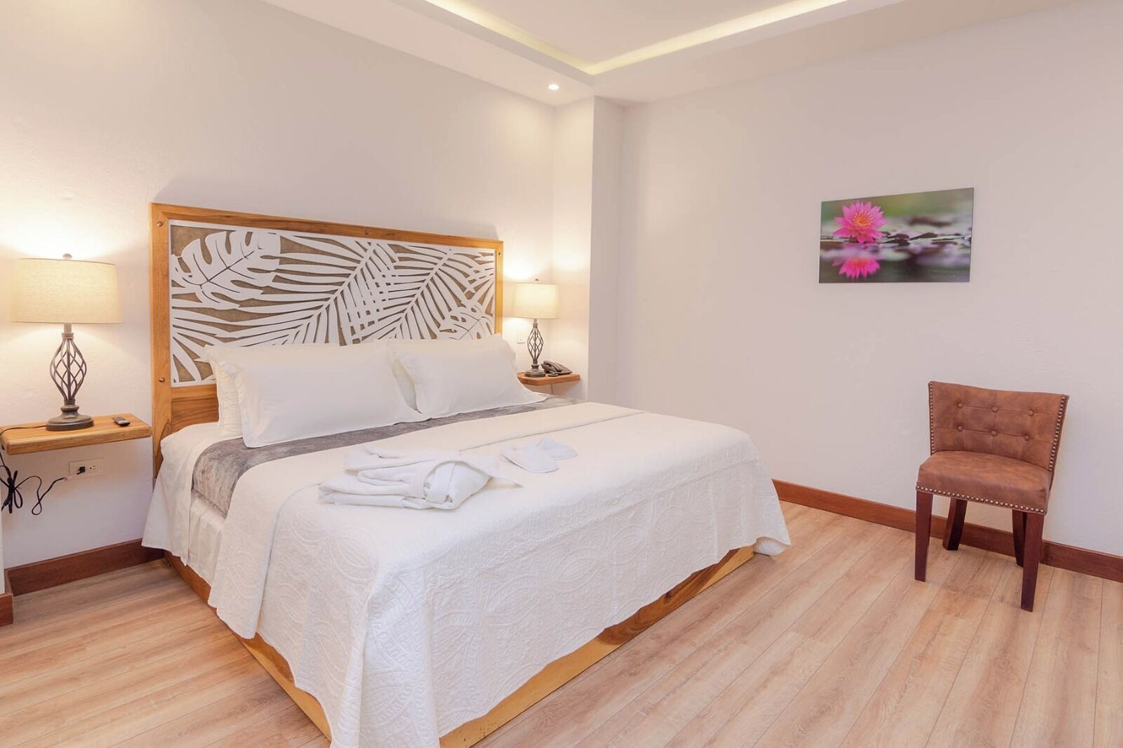 A hotel room with a large bed, two bedside tables, a chair, and a wall-mounted artwork.