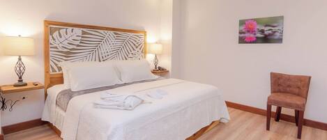 A hotel room with a large bed, two bedside tables, a chair, and a wall-mounted artwork.