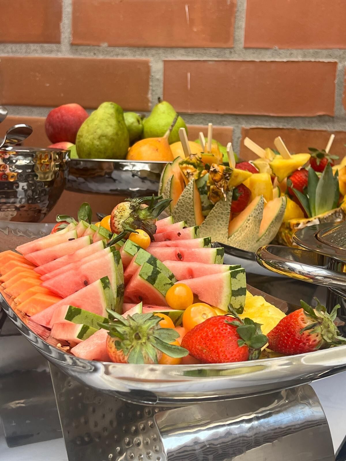 Un bufé con diversas frutas y una bandeja de metal.