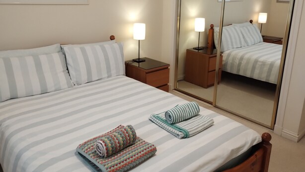 A hotel room with a bed, two bedside tables, a mirror, and a wall-mounted painting. - Central 2-Bedroom Apartment with private parking - home from home (Edinburgh)