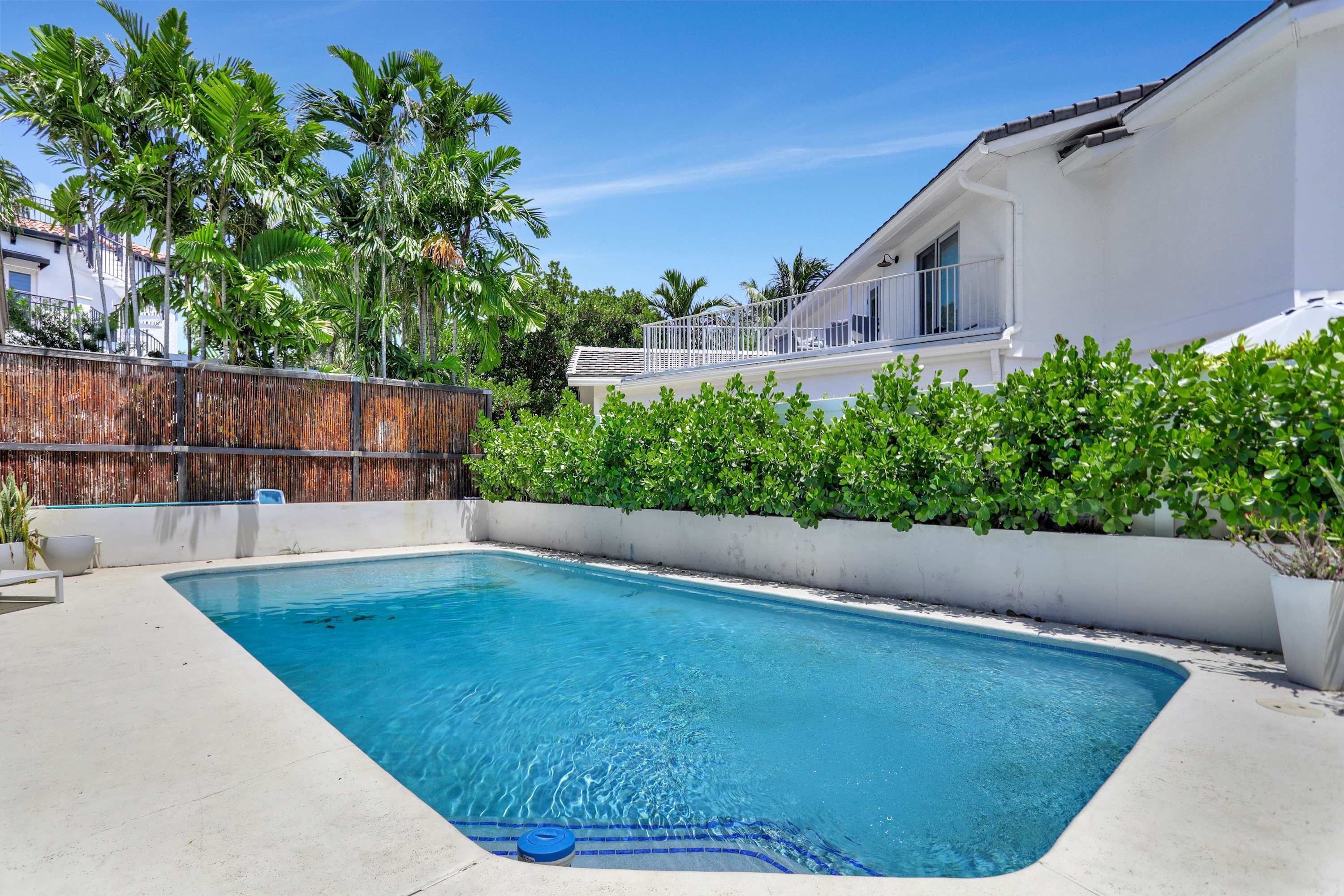 A swimming pool with a wooden fence, surrounded by lush greenery and a white building with balconies.