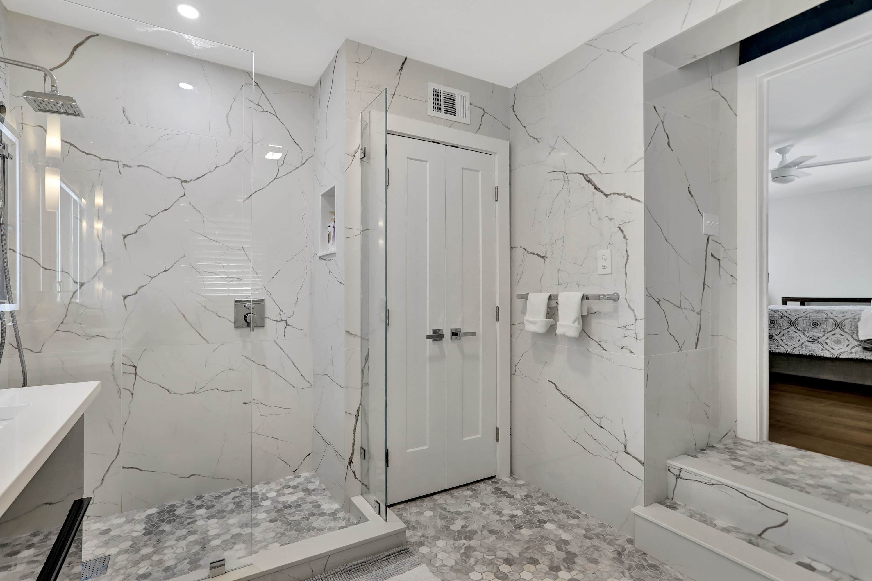 A modern bathroom with marble walls, a glass shower enclosure, and a white vanity.