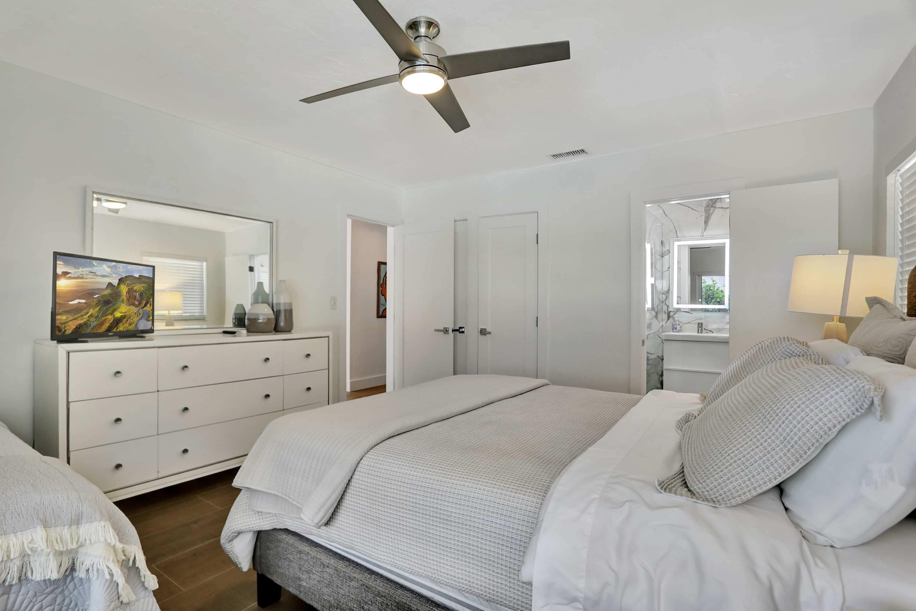 Ein Schlafzimmer mit Bett, Kommode, Spiegel und Deckenventilator.