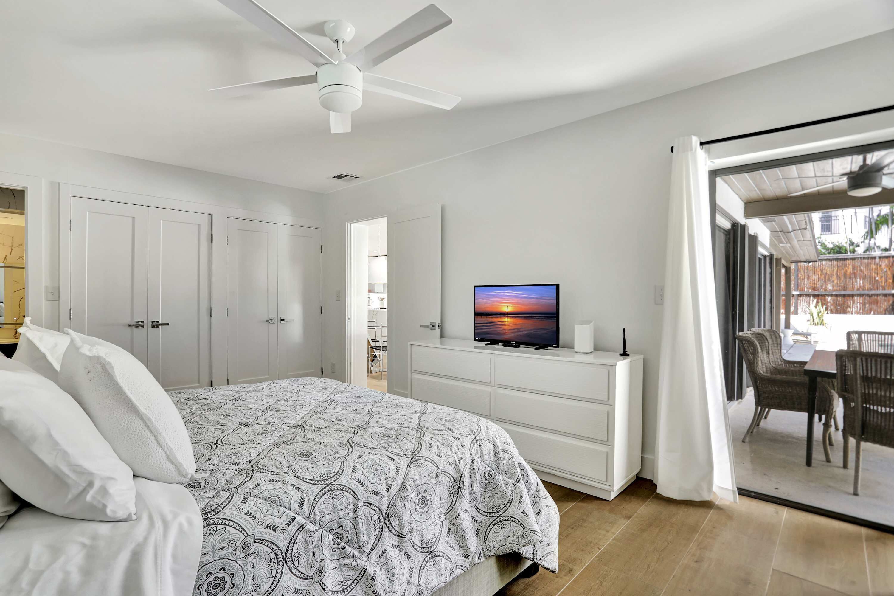 A bedroom with a bed, a TV, a ceiling fan, and a sliding glass door to a balcony.