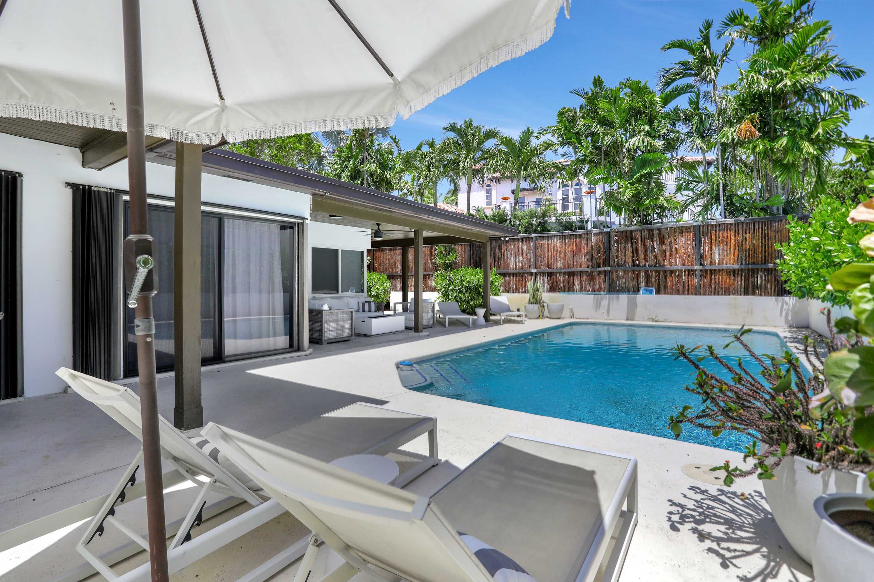 Ein Poolbereich mit Liegestühlen, einer überdachten Lounge und Blick auf ein Wohngebäude im Hintergrund.