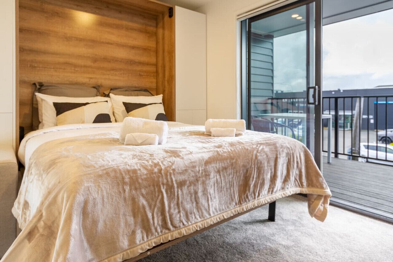 Un dormitorio con una cama grande, cabecera de madera y vistas al balcón exterior.