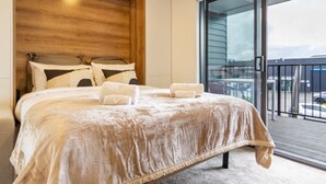 A bedroom with a large bed, a wooden headboard, and a view of the outside balcony. - Luxurious Studio: Prime location, City Centre (Christchurch)