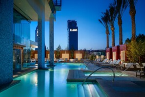 Une piscine d’hôtel avec des chaises longues, et en arrière-plan, un grand bâtiment sur lequel on peut lire l’inscription « PALMS ».