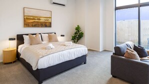A modern bedroom with a large bed, a grey sofa, and a large window. - Single Level Studio, CBD Escape: King bed (Christchurch)