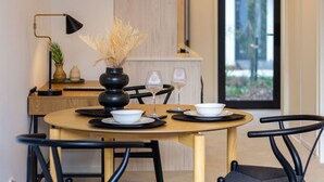 A dining area with a round table set for two, featuring black chairs, white plates, and a vase with dried plants. - Single Level Studio, CBD Escape: King bed (Christchurch)