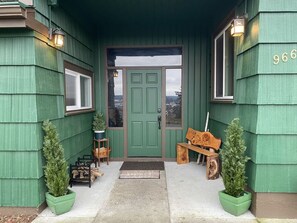 A green building with a green door, a bench, and two potted plants.