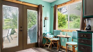 Une pièce dotée d’une porte-fenêtre coulissante, d’une petite table avec des chaises, d’un banc et d’un meuble.