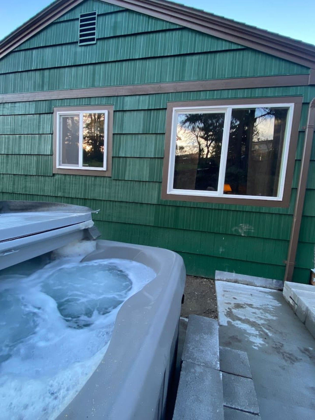 Una casa con un jacuzzi en primer plano, una ventana y una chimenea.