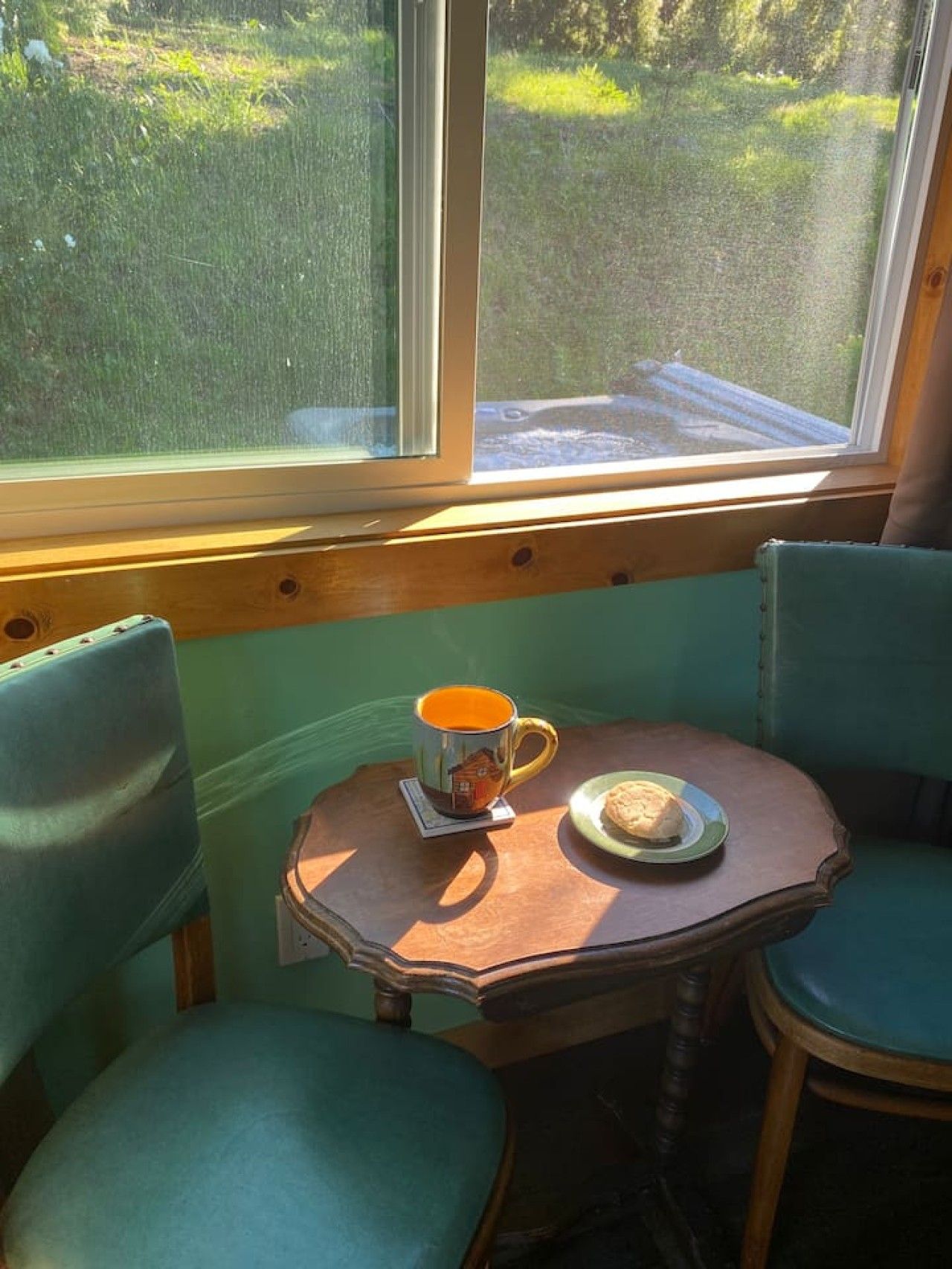 A corner seating area with a table, two chairs, a mug, and a plate with a biscuit.